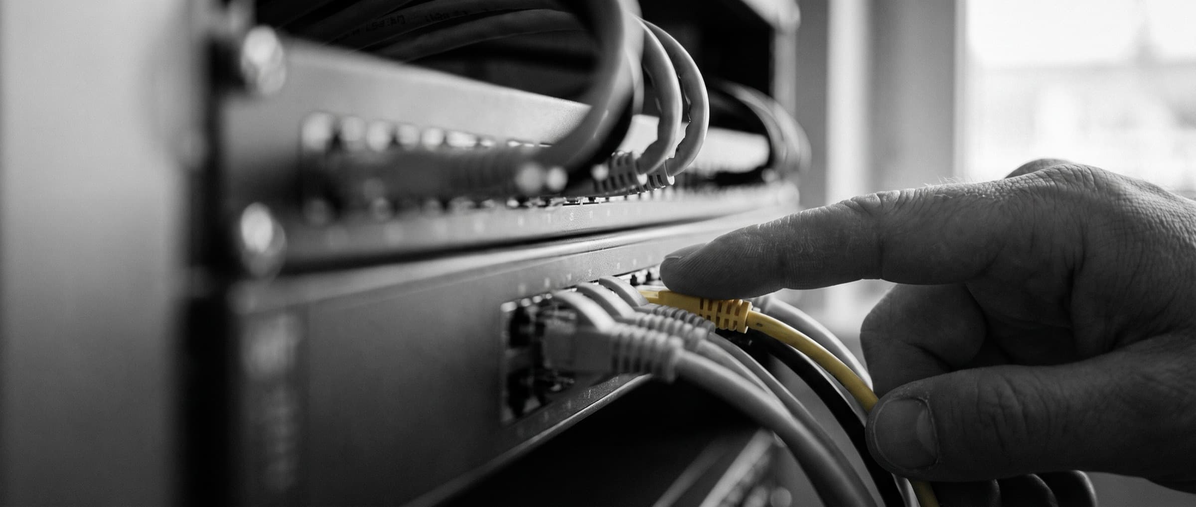 A hand tracing a single yellow network cable to a port on a modern switch